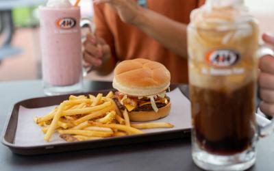 Two people sitting across from each other at an A&W. There is a burger and fries on the plate and one is having a milkshake and the other is having a root beer float.