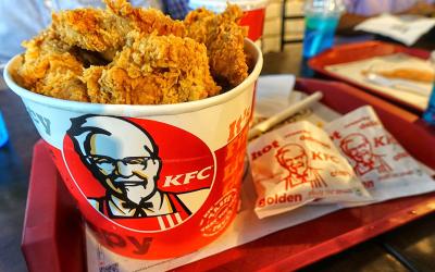 A KFC-branded bucket of chicken with fries served on a plastic tray.